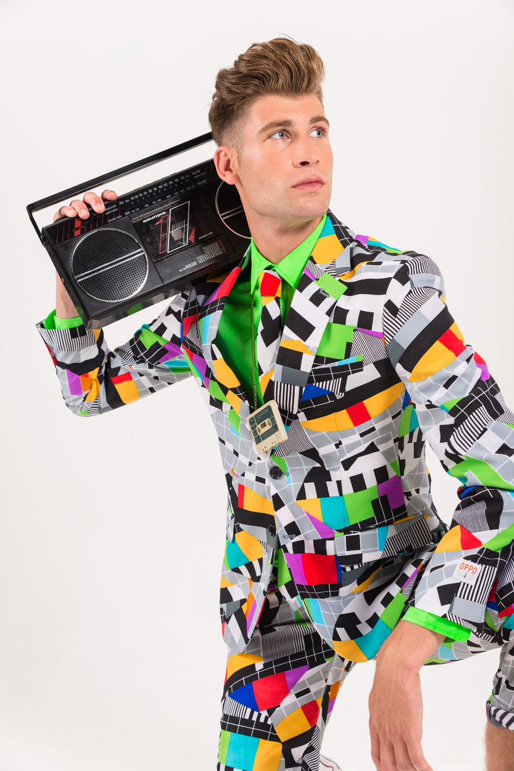 Man wearing a colorful test-pattern suit and matching tie while holding a retro boombox over his shoulder.