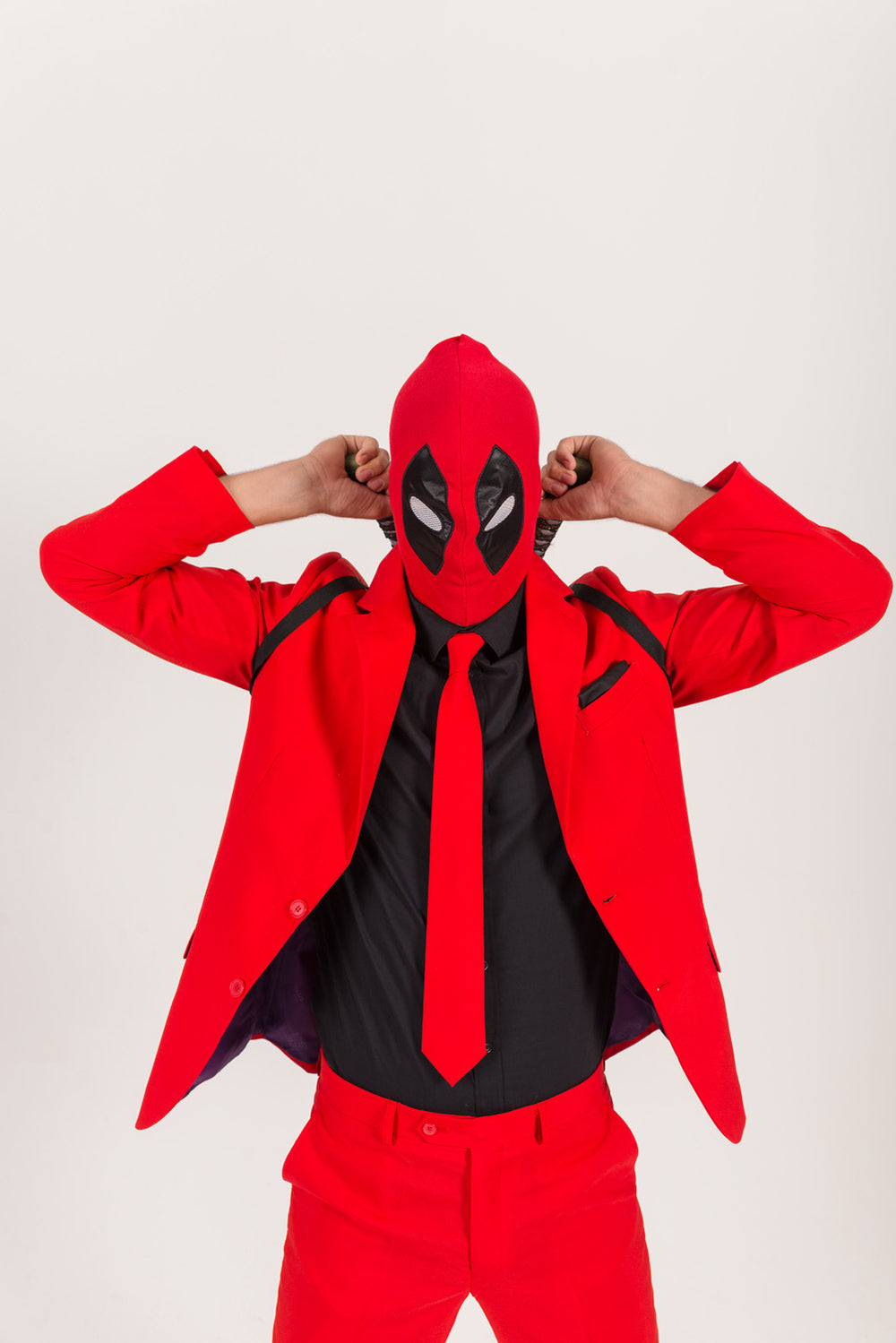 Person in a red suit, black shirt, and red tie wearing a red-and-black superhero-style mask with hands behind their head.