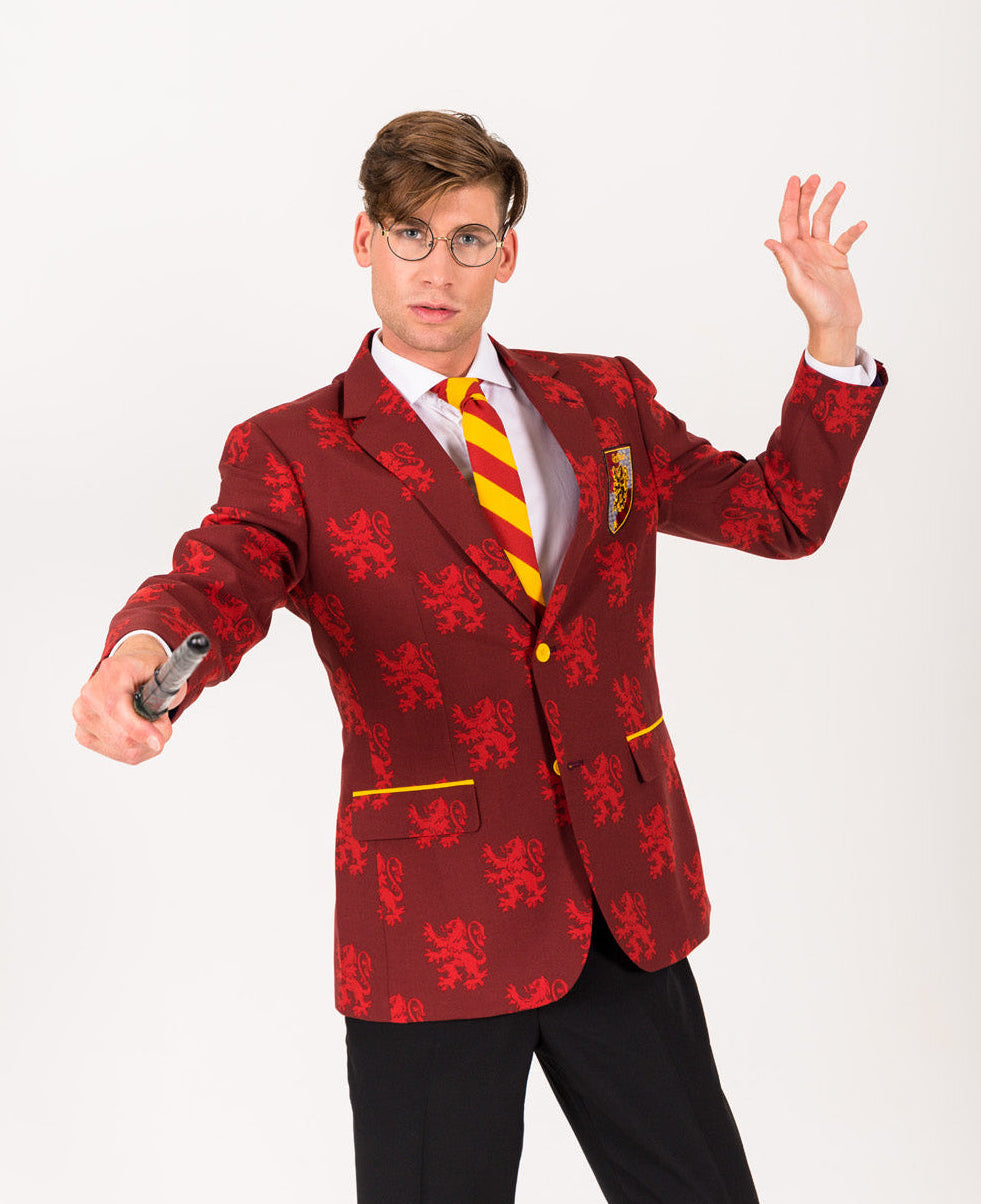 A man wearing a red and dark red patterned blazer with a yellow and red striped tie, white shirt, and black trousers, posing against a white studio background while holding a toy gun.
