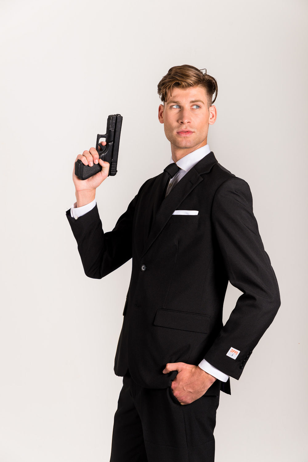 Man in a black suit and tie holding a handgun upright beside his shoulder, imitating James Bond