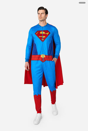 A man modeling a Superman-themed full-zip one-piece costume against a light gray studio background. The costume is bright blue with red and yellow details, including a large Superman 'S' shield on the chest, a red cape, a red waist belt, and red boot covers.