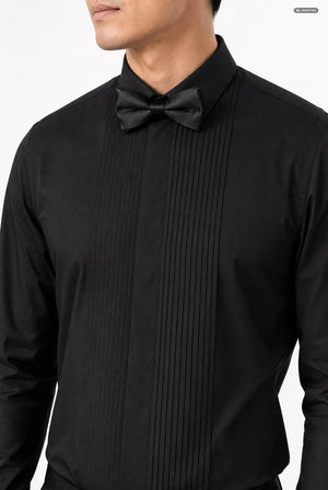 A close-up of a man wearing a black long-sleeve pleated tuxedo shirt with a matching black bow tie, shown against a plain white background.