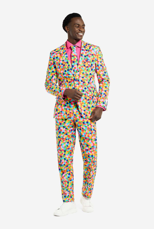 Man wearing men's suit with multicolor all-over confetti print and pink dress shirt. Suit consist of jacket, pants and tie. Full body image.