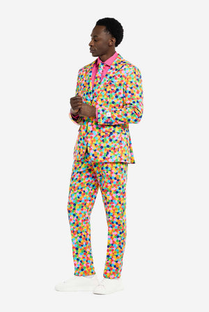 Man wearing men's suit with multicolor all-over confetti print and pink dress shirt. Suit consist of jacket, pants and tie. Full body image, side view.