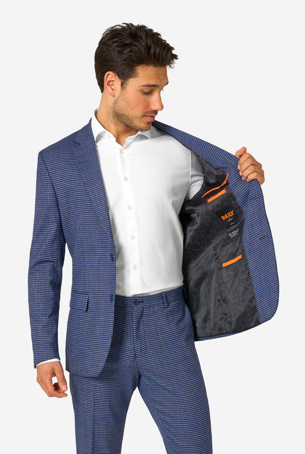 Man wearing a blue checkered suit with a white shirt, holding open his jacket to reveal a branded interior.