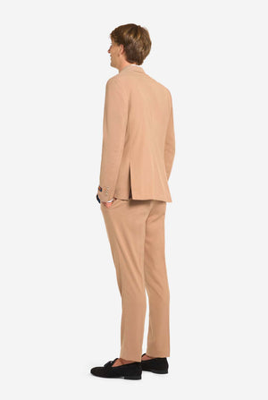 Person wearing a beige suit standing against a white background