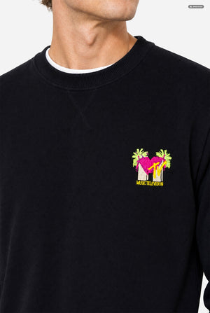A close-up of a person wearing a black crewneck sweatshirt with a colorful embroidered MTV graphic on the left chest. 