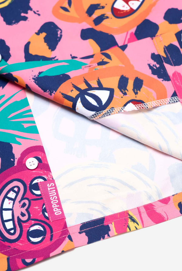 Image of a vibrant two-piece summer outfit featuring a bold tropical print. The short-sleeve button-up shirt and matching shorts showcase a lively design with neon pink, orange, and yellow leopard prints, bananas, green palm leaves, and quirky cartoon faces. The outfit is styled casually with a green T-shirt underneath and is perfect for summer parties, vacations, or poolside fun. Shirt close up.