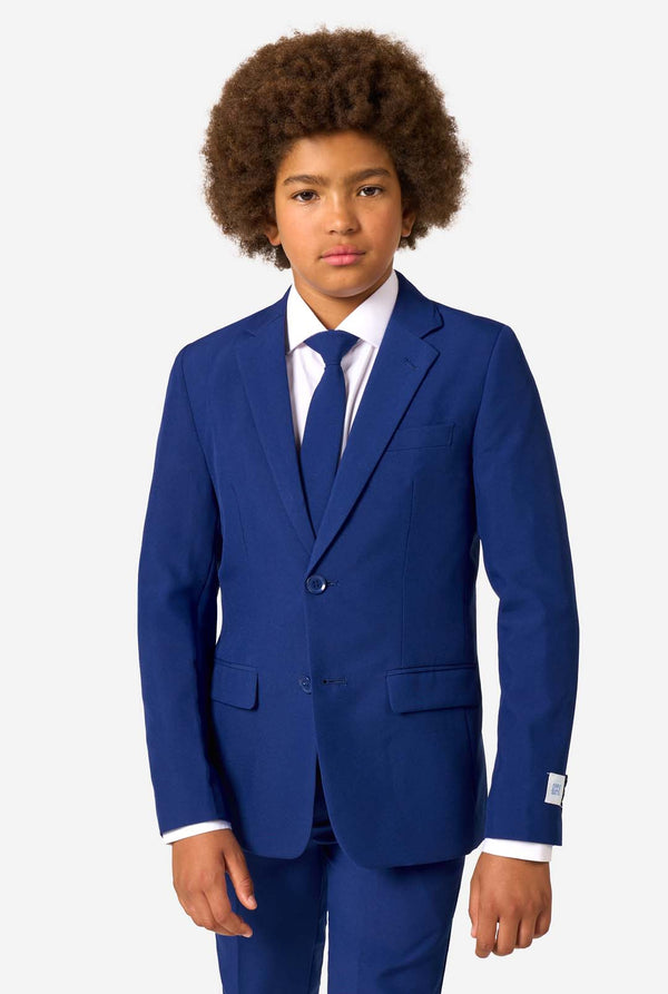 Kid wearing a navy blue suit with a white shirt and tie on a light gray background.