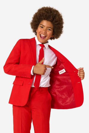Child wearing a red suit with a tie, pointing to the chest pocket.