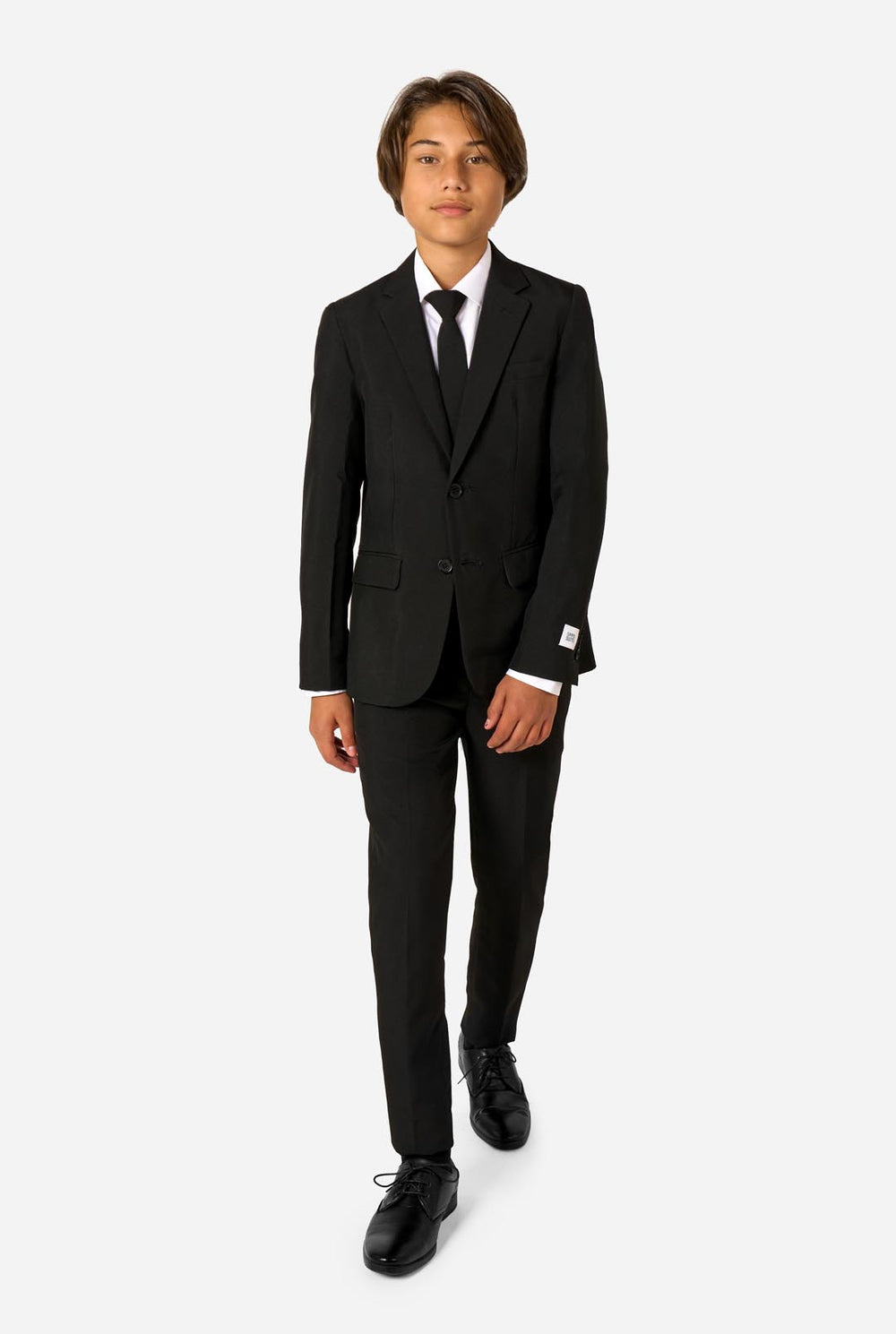 Teenager wearing a black suit and a white shirt on a light background.