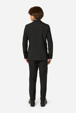 Teenager wearing a black suit and a white shirt on a light background. View from the back.