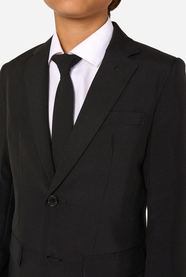 Teenager wearing a black suit and a white shirt on a light background. Chest close up.