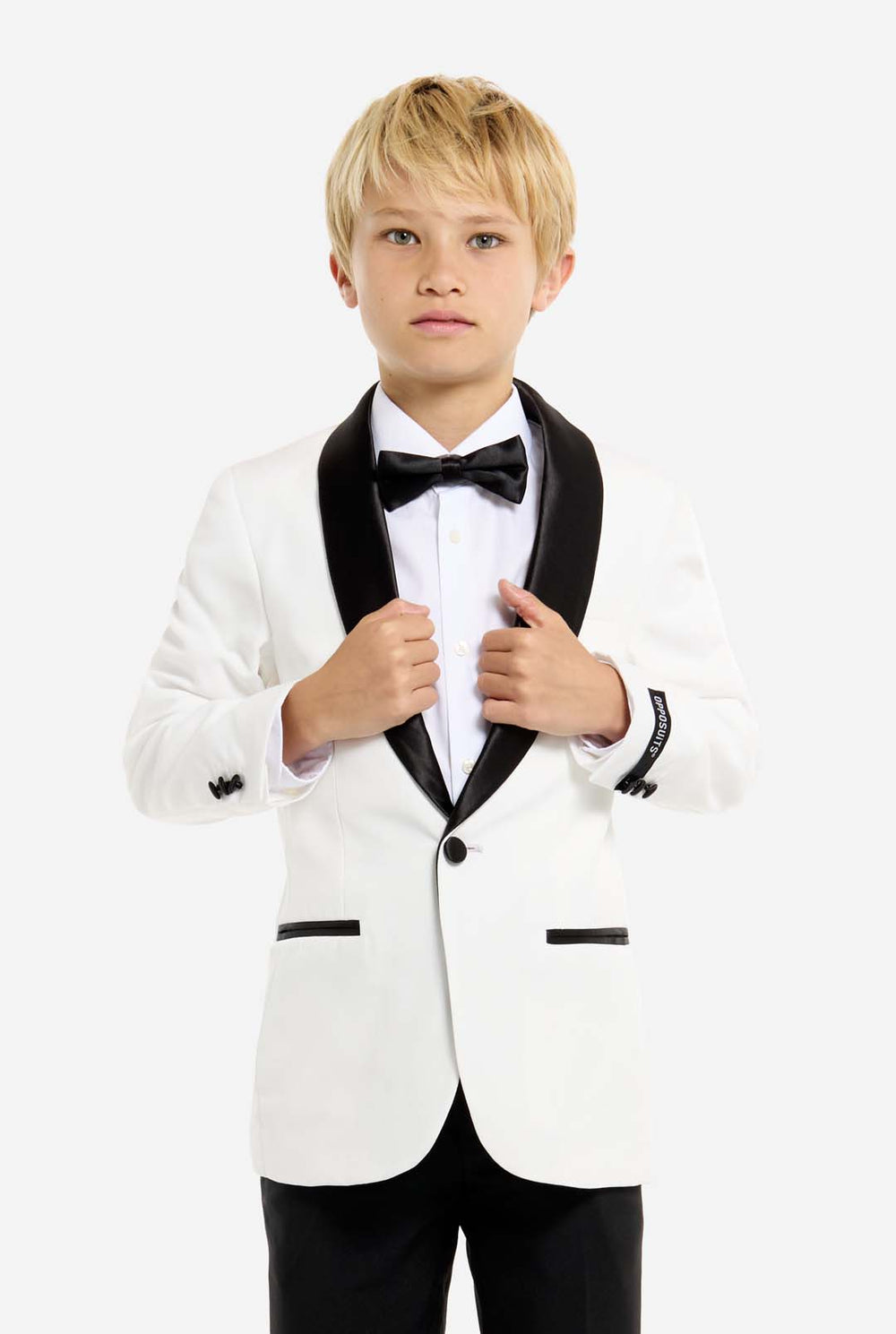 Young boy wearing a white tuxedo with black bow tie and pants on a white background