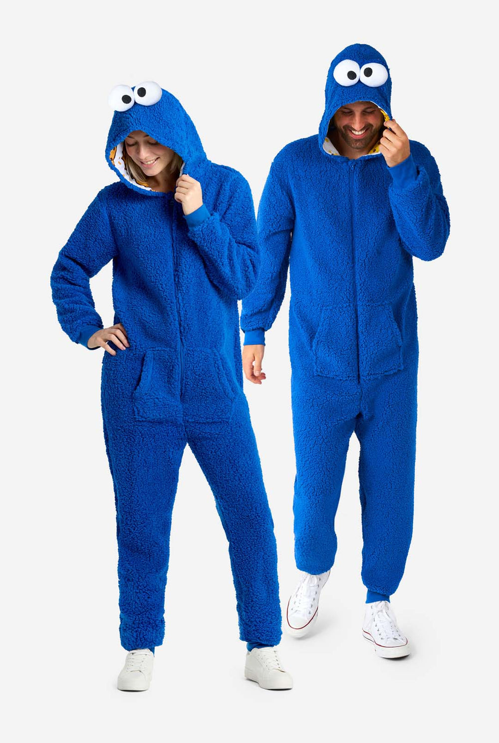 Man and Woman wearing blue pluche Cookie Monster Adult onesie for adults. Standing next to each other, holding hood with hands.