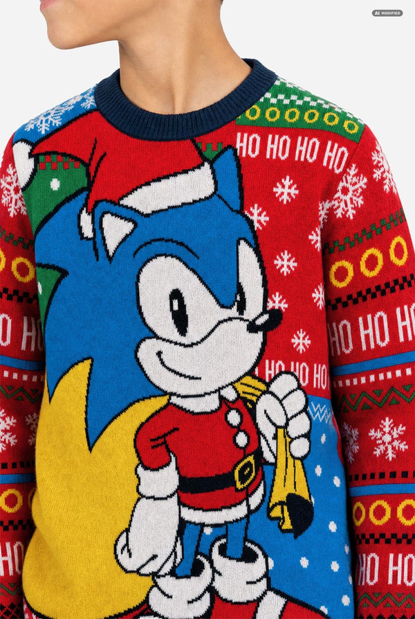 A close-up of a person wearing a festive holiday sweater featuring Sonic the Hedgehog. The sweater has a red crew neck and is decorated with a large graphic of Sonic in Santa's suit, a yellow gift bag, and 'HO HO HO' text and snowflake patterns on a red background.