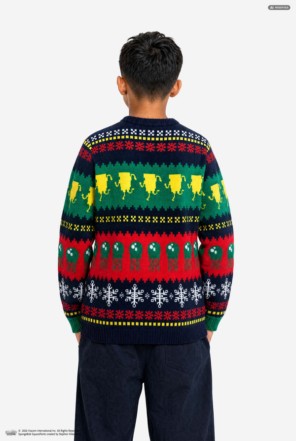 A child viewed from behind wearing a long-sleeve crewneck sweater with a colorful Nordic pattern featuring reindeer, snowflakes, and geometric stripes in green, red, yellow, and navy blue.
