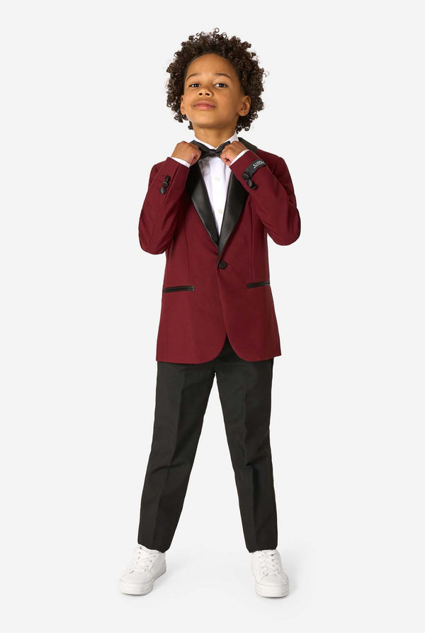 Child wearing a burgundy tuxedo with black lapels on a white background. Full body image.