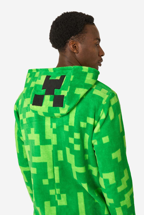 Person wearing a green pixelated Creeper onesie with a black logo on a white background