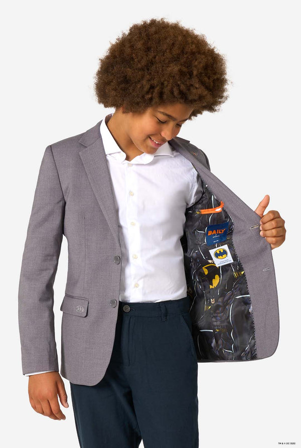 A child opening a grey blazer to show the inner lining with Batman comic graphics.