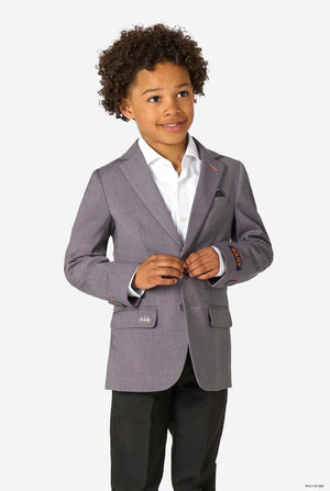 A young boy wearing a light grey blazer, white shirt, and black trousers, smiling while buttoning his jacket.