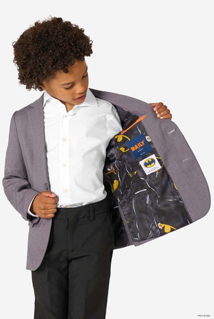 A young boy in a grey blazer looking down, showing the inside lining printed with Batman logos and patterns.