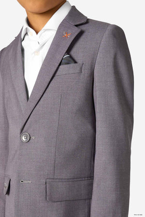 Close-up of the upper part of a grey blazer, showing a small orange cross-stitch pin and a pocket square.
