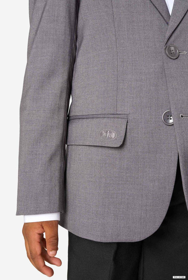 Close-up of the lower part of a grey blazer showing a flap pocket embroidered with a subtle Batman logo.