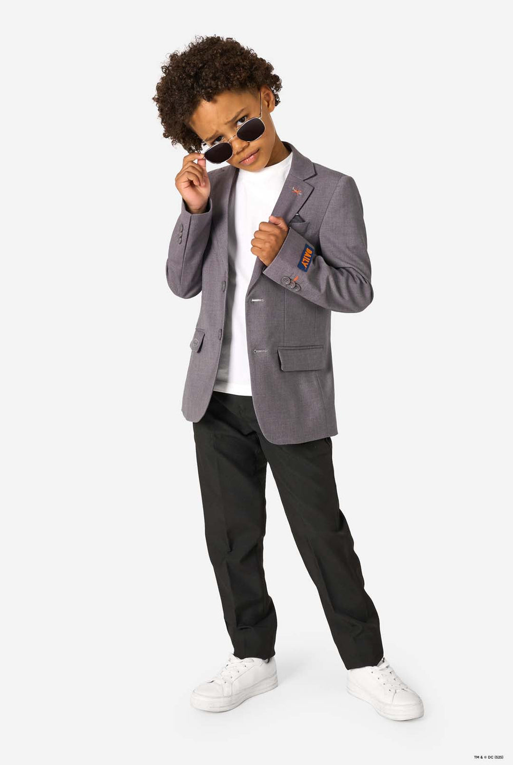 A young boy wearing a light grey blazer, white shirt, and black trousers, smiling while buttoning his jacket.