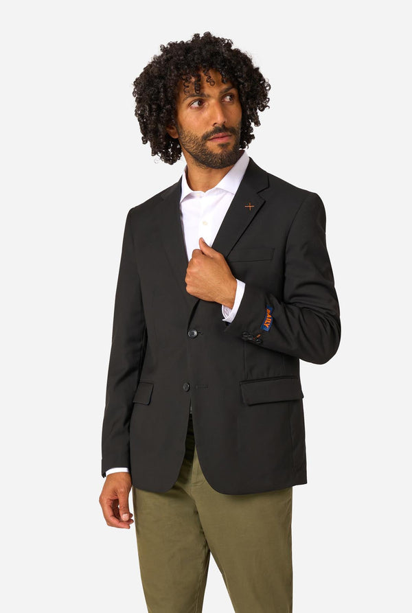 Man wearing a black blazer over a white shirt with green pants on a white background