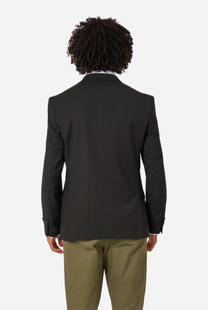 Person wearing a black blazer and beige pants on a white background. View from the back.