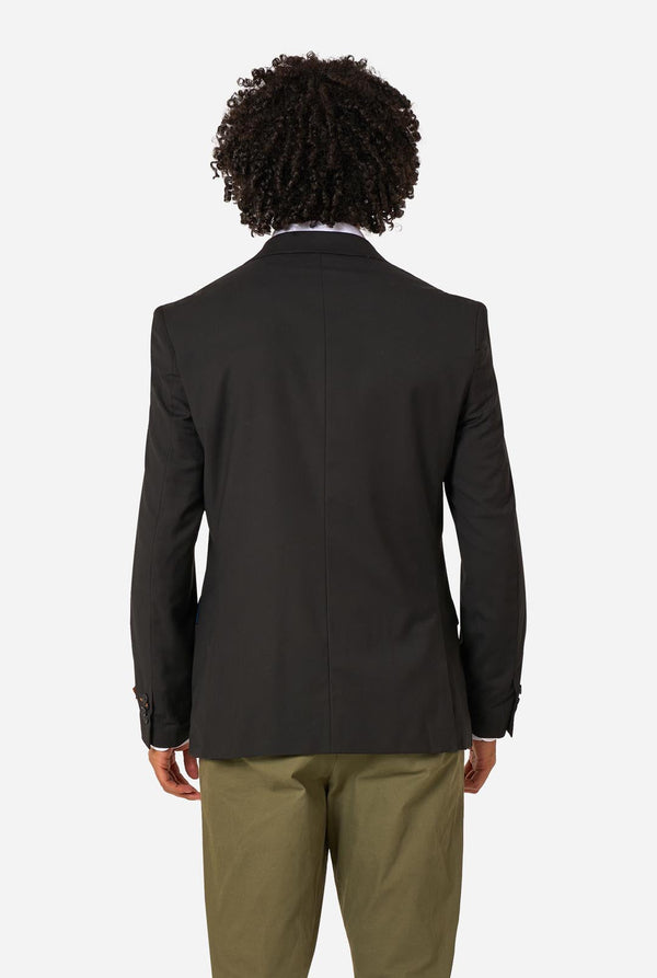 Person wearing a black blazer and beige pants on a white background. View from the back.