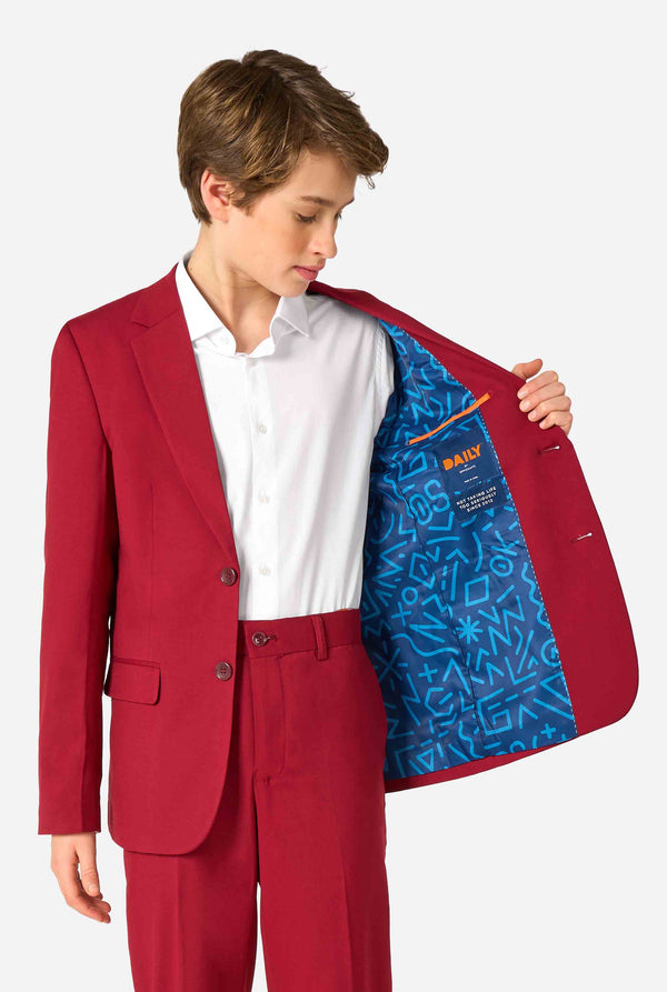 Teen boy wearing a stylish burgundy red suit with a white dress shirt, looking confidently. Perfect formal outfit for boys' special occasions, weddings, and parties.Holding one side of the jacket open.