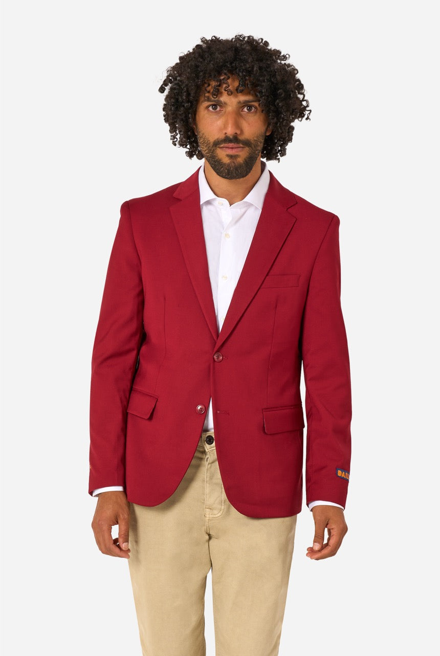 Man wearing a red blazer over a white shirt with beige pants on a white background