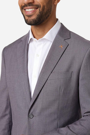 Man wearing a gray suit jacket over a white shirt on a plain background. Close up of the chest.