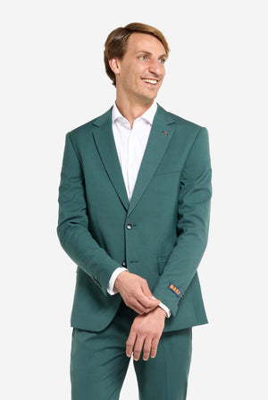 Image with light grey background and man wearing dark green men’s suit and white shirt. Suits consists of blazer and pants. Man looking side ways.