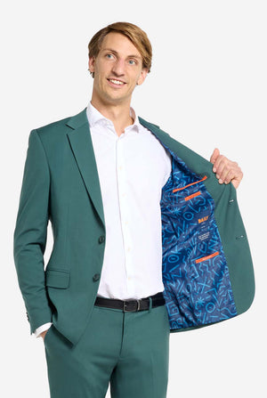 Image with light grey background and man wearing dark green men’s suit and white shirt. Suits consists of blazer and pants. Man looking side ways and holding one hand in his pocket and one side of the jacket open.