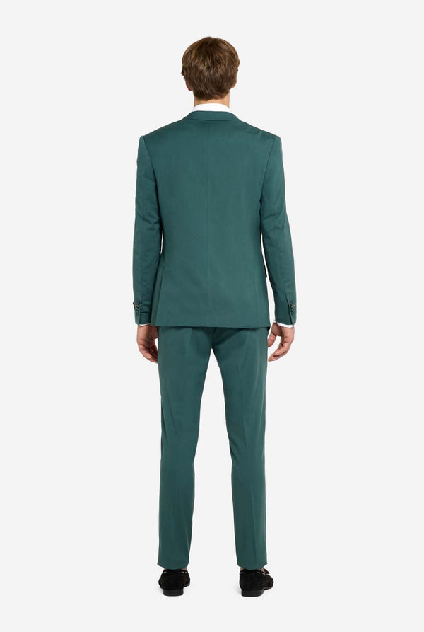 Image with light grey background and man wearing dark green men’s suit and white shirt. Suits consists of blazer and pants. Man facing away from the camera and showing the back of the suit. 