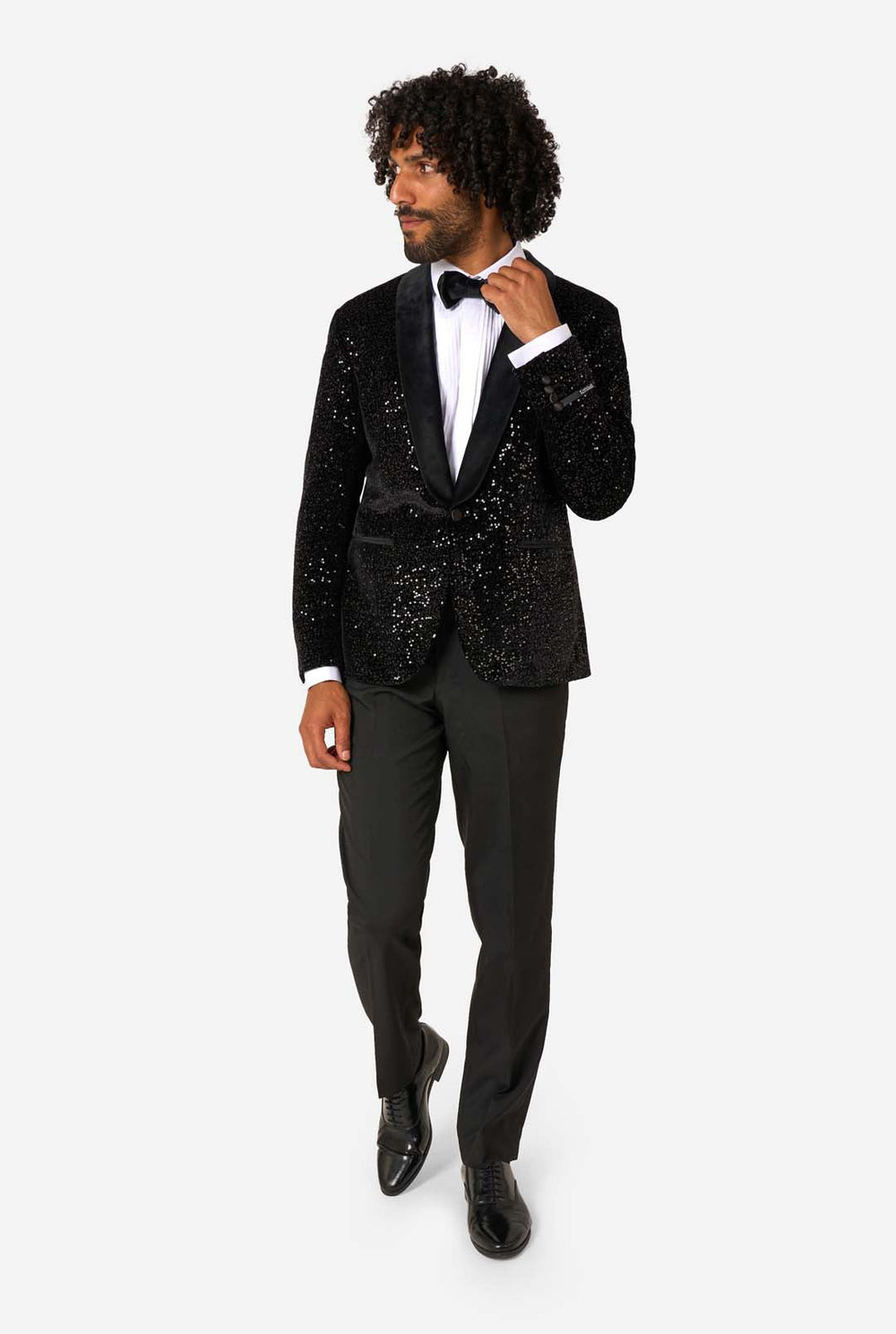 Man wearing a black sequin jacket with a white shirt and bow tie on a white background.