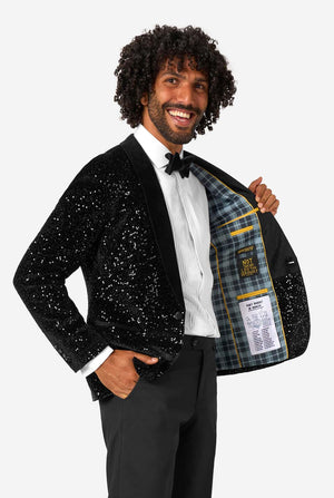 Man wearing a black sequin jacket with a plaid lining, smiling against a white background