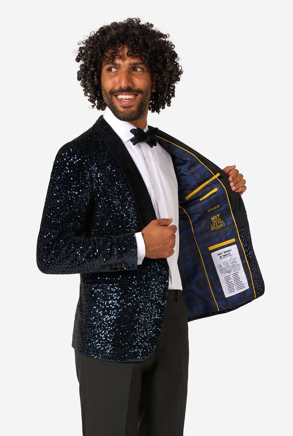 Man wearing a sparkling blue blazer with a label, standing against a white background