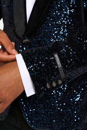 Close-up of a navy sequin suit jacket with a hand adjusting the cuff, featuring the brand 'Bodysuit'.