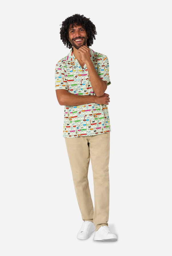 Man wearing a colorful Monopoly patterned shirt and beige pants on a white background. Full body image