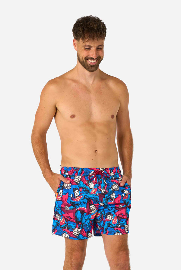 Man wearing colorful patterned Superman-themed swim shorts on a white background