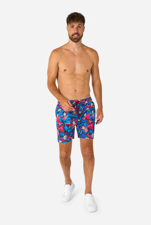 Man wearing colorful Superman-themed swim shorts on a white background