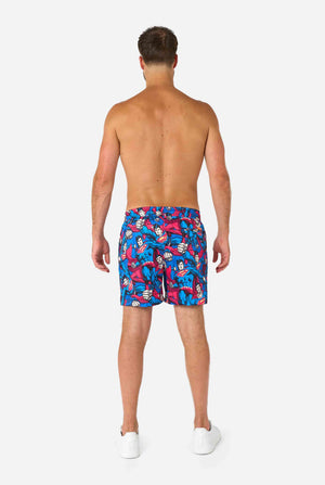 Man wearing colorful Superman-themed swim shorts on a white background
