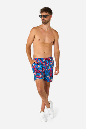 Man wearing colorful Superman-themed swim shorts on a white background