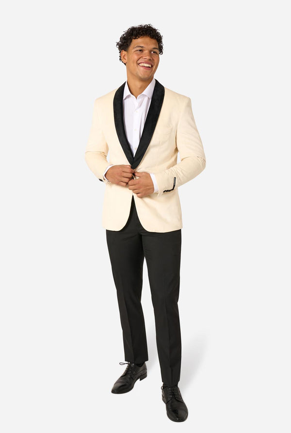 Man wearing a cream blazer with black lapels and black pants on a light background. Full body image.