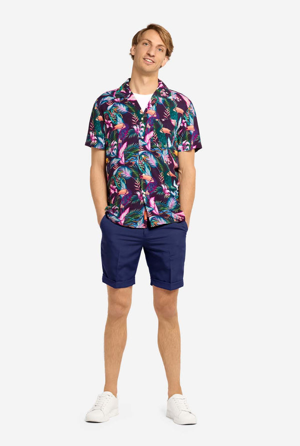 Man wearing a colorful floral shirt and navy shorts on a white background. Full body image