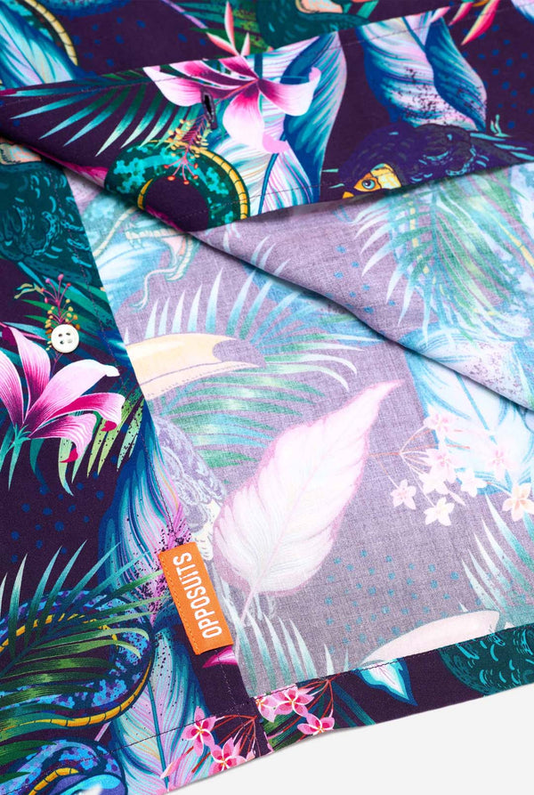 An image of a purple Hawaiian shirt with a tropical print, resembling the jungle night live. The print consists of parrots, snakes, leaves, and flowers. Close up.